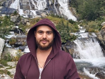 Mohammad wearing a burgundy hoodie while standing in front of a waterfall