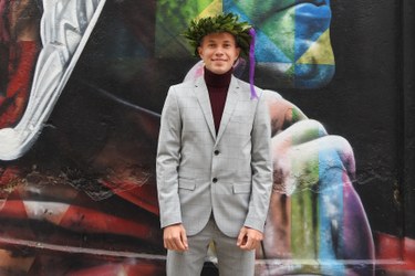 Dmytro standing in front of mural art on his graduation day